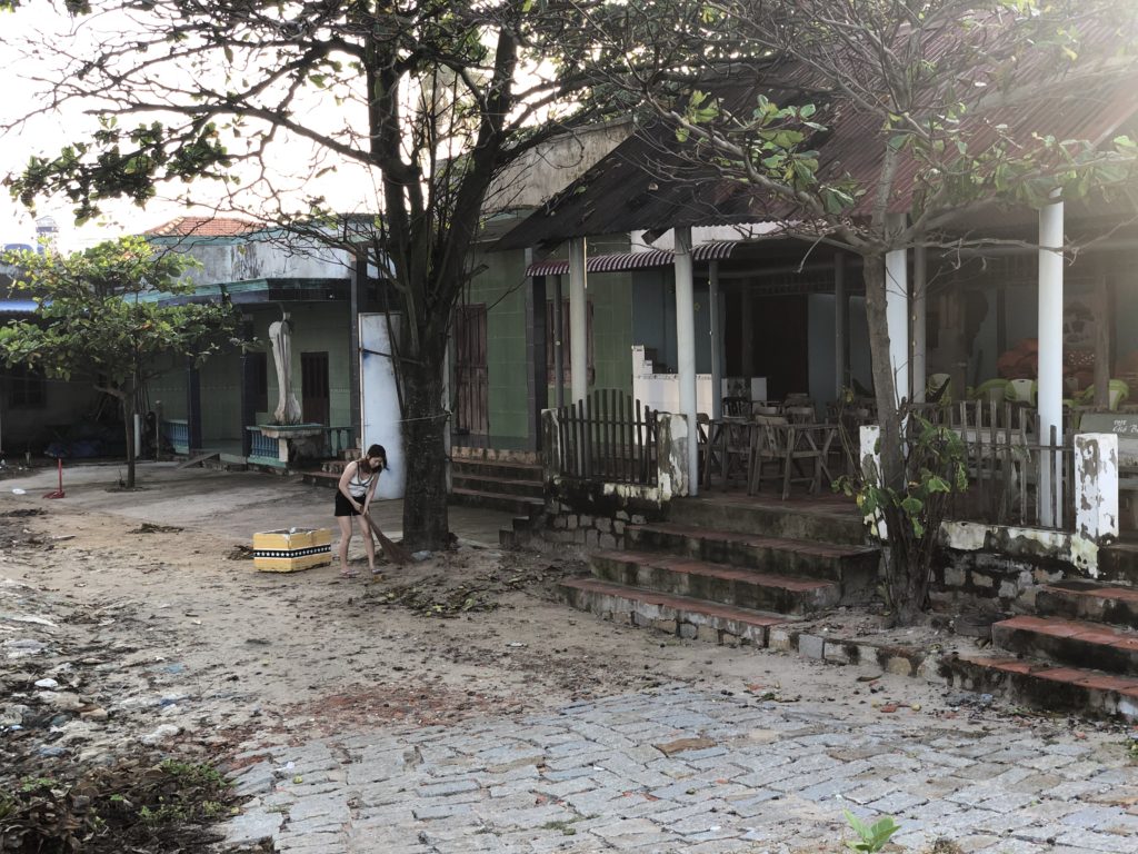 Vietnamese woman sweeping up dead leaves and rubbish with a wooden broom