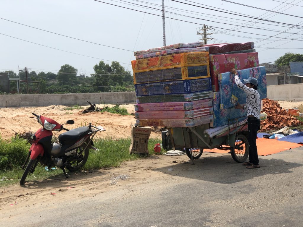 Vietnamese loading a large number of mattresses onto a motorbike